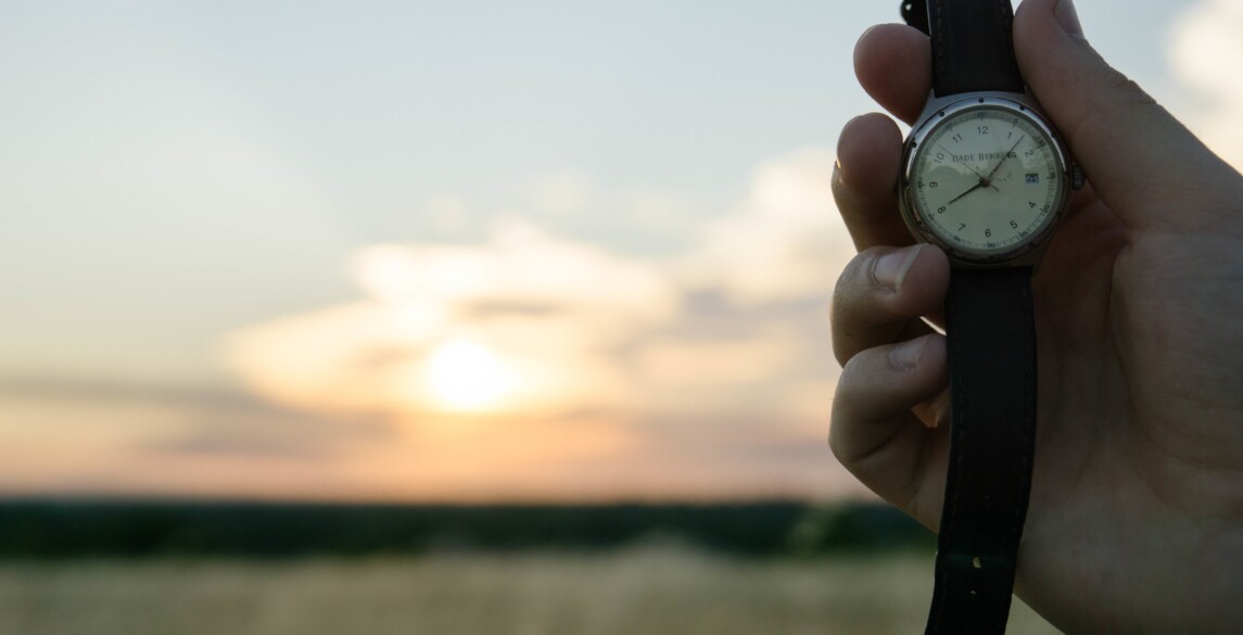 Person holding a watch with sunset in the background