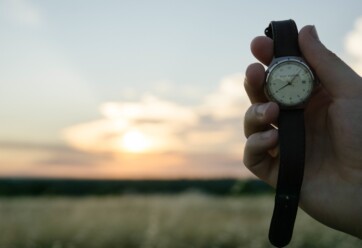 Person holding a watch with sunset in the background