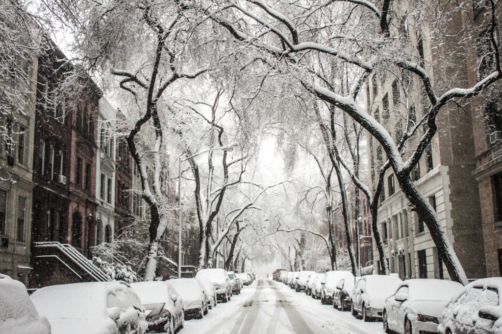 Street covered in snow with homes and cars on either side