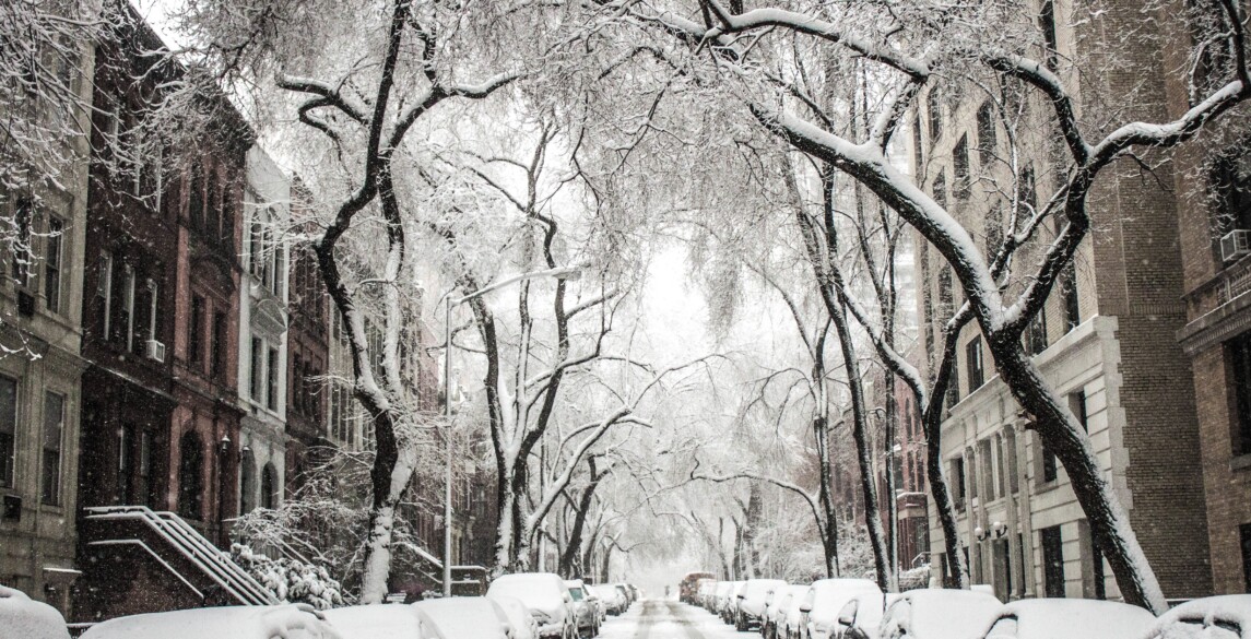 Street covered in snow with homes and cars on either side