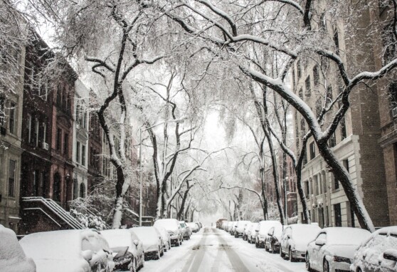 Street covered in snow with homes and cars on either side
