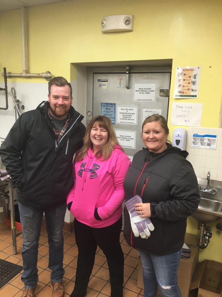 Hilldrup employees smile by a freezer located at the homeless shelter