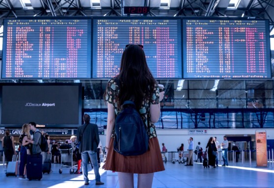 Girl standing back facing the camera in an airport toward the flight information display system