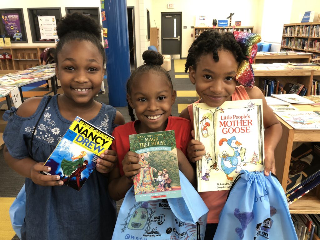 Three girls holding up books smiling