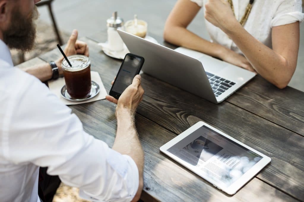 Two people at a table, one looking at a phone and the other at their laptop