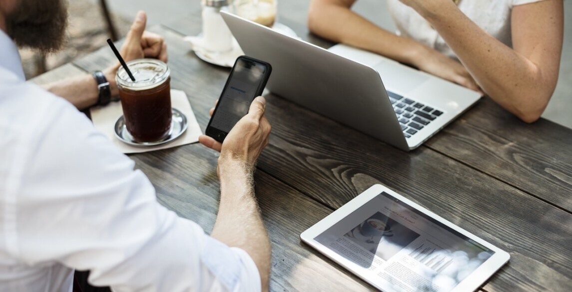 Two people at a table, one looking at a phone and the other at their laptop