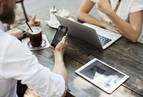 Two people at a table, one looking at a phone and the other at their laptop