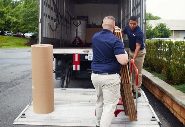 Two movers use a lift gate to put items into a truck