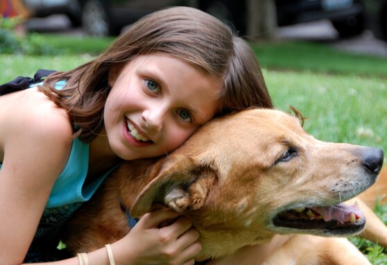 Young girl embracing pet dog.