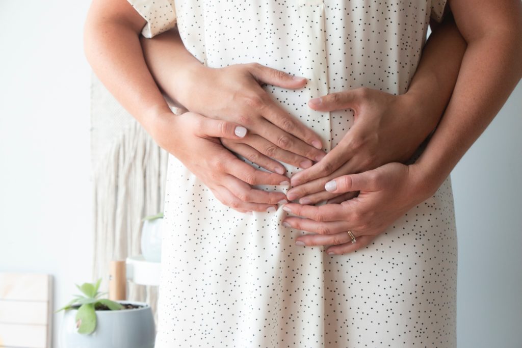 Pregnant couple embracing pregnant belly.