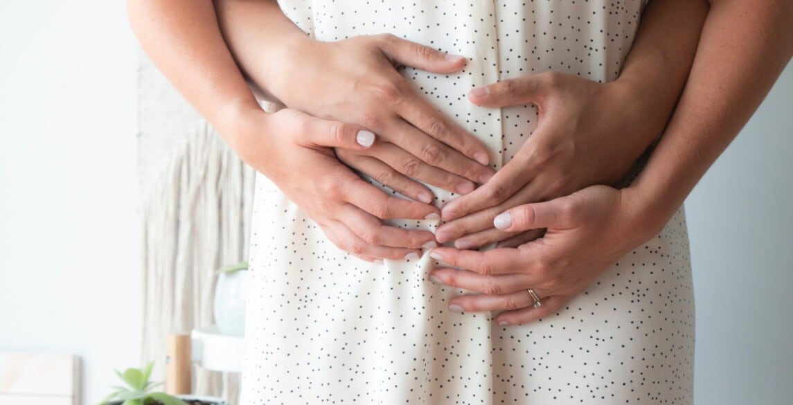 Pregnant couple embracing pregnant belly.