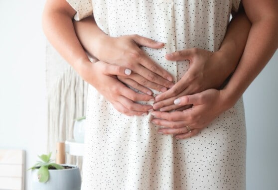 Pregnant couple embracing pregnant belly.