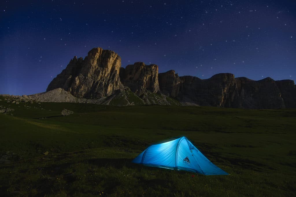 Blue tent in a field near the mountains on a starry night