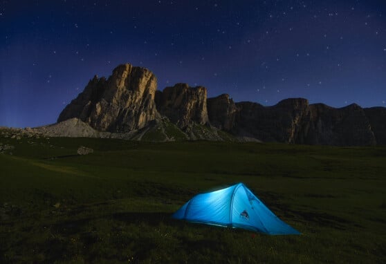 Blue tent in a field near the mountains on a starry night