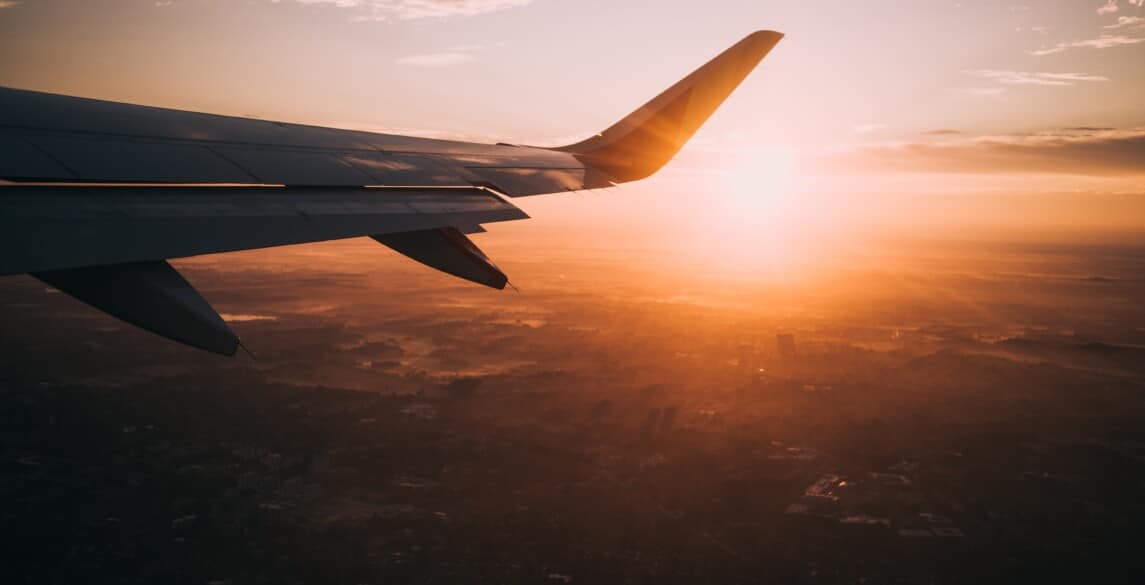 The wing of a plane with the sun setting behind