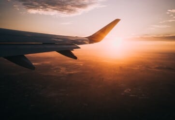 The wing of a plane with the sun setting behind