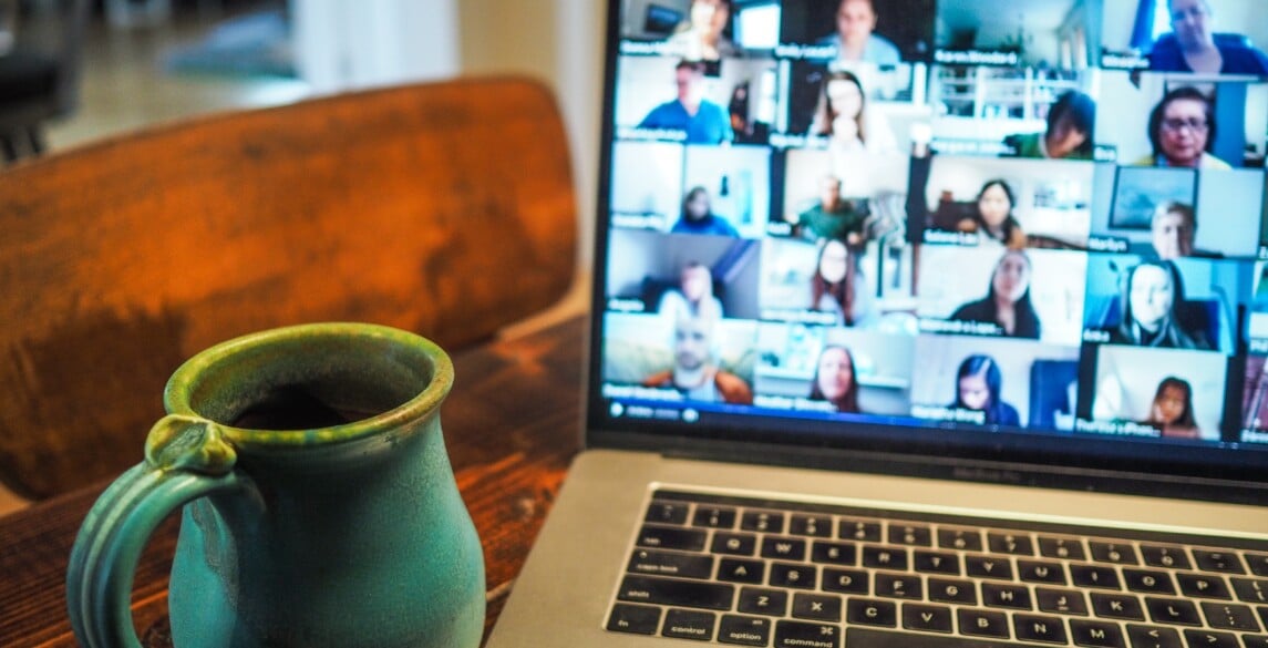 Picture of a desk with a coffee mug and a laptop with a Zoom screen up.