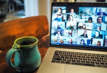 Picture of a desk with a coffee mug and a laptop with a Zoom screen up.