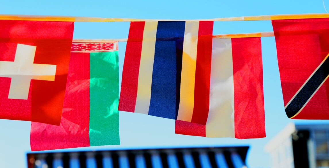 Different international flags hanging against a blue sky.