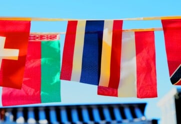 Different international flags hanging against a blue sky.