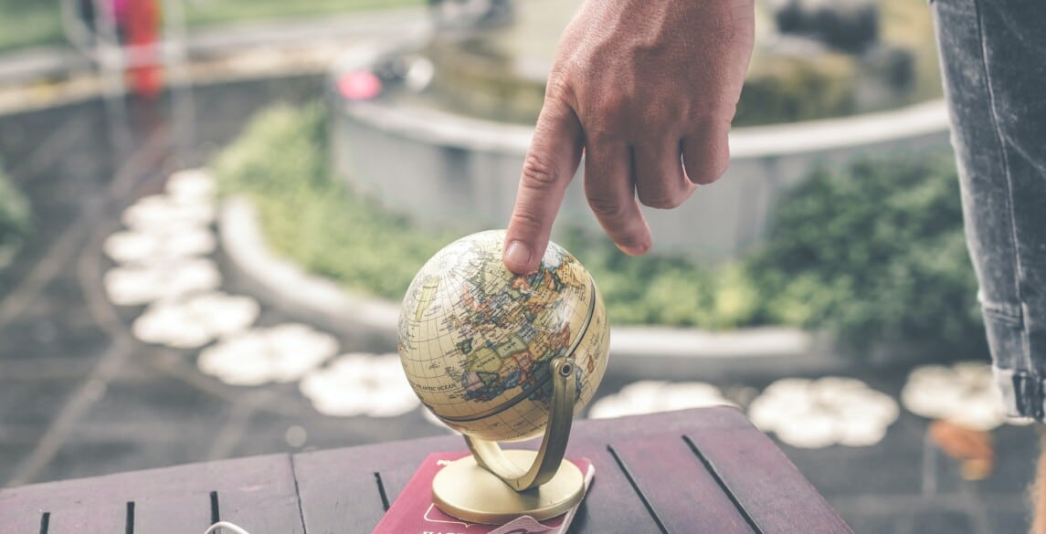 Person touching a small globe that is sitting on a table.