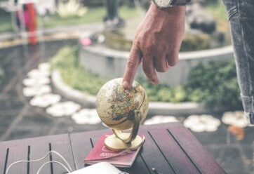 Person touching a small globe that is sitting on a table.