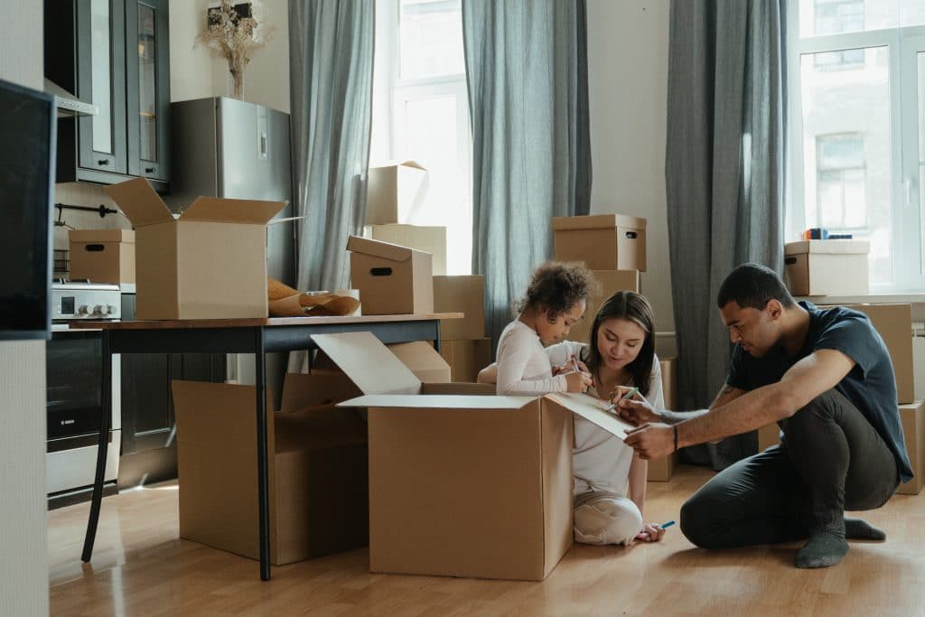 Two adults and one small child gathered around moving boxes in a kitchen.