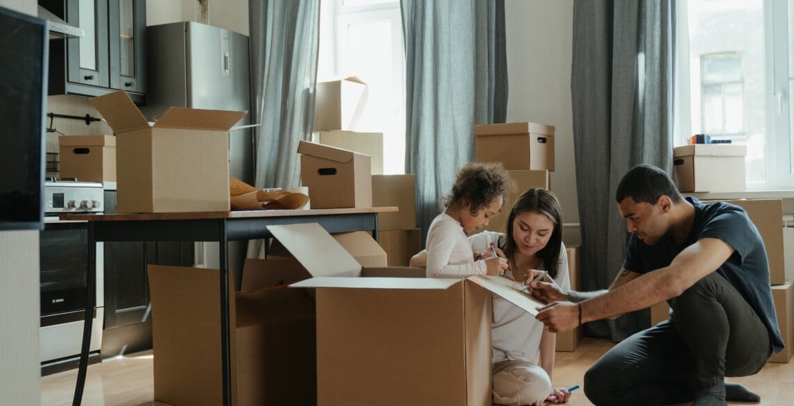 Two adults and one small child gathered around moving boxes in a kitchen.