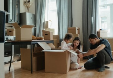 Two adults and one small child gathered around moving boxes in a kitchen.
