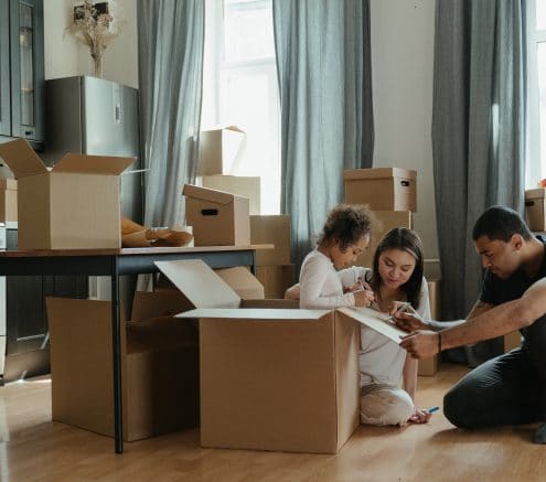Two adults and one small child gathered around moving boxes in a kitchen.