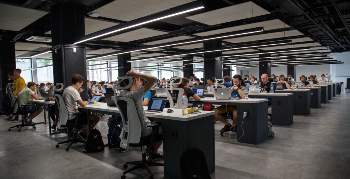 Open office with rows of tables, computers and employees.