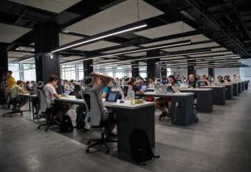 Open office with rows of tables, computers and employees.