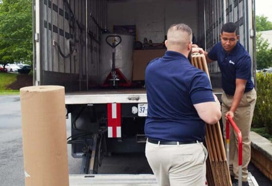 Two men unloading a large item from a moving truck.