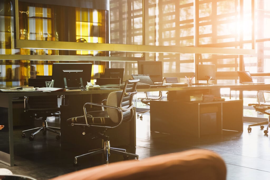 Light shining in on modern office with communal workspace and rolling chairs