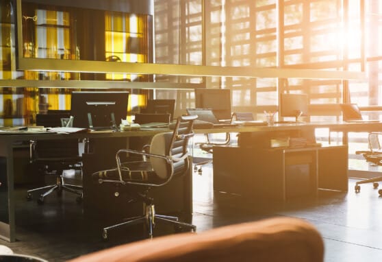 Light shining in on modern office with communal workspace and rolling chairs