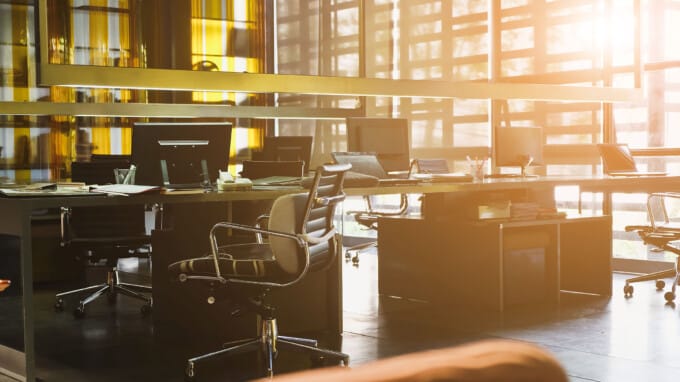 Light shining in on modern office with communal workspace and rolling chairs