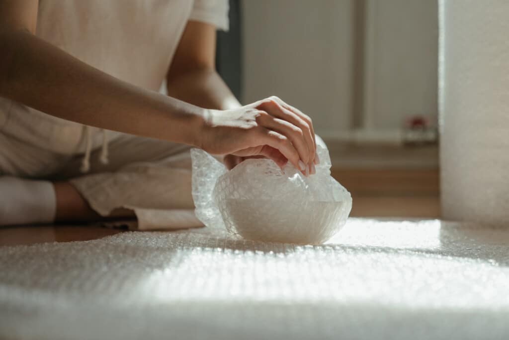 Person wrapping bowl with bubble wrap.