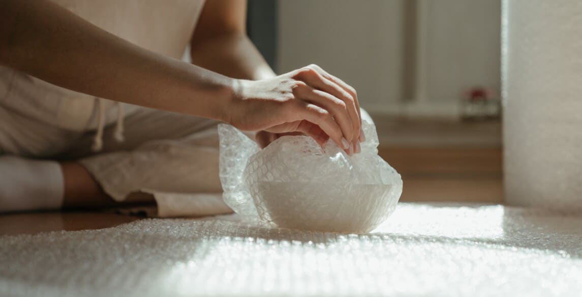 Person wrapping bowl with bubble wrap.
