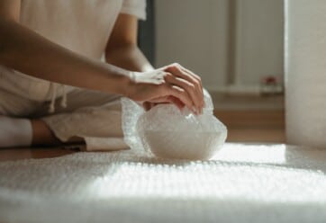 Person wrapping bowl with bubble wrap.