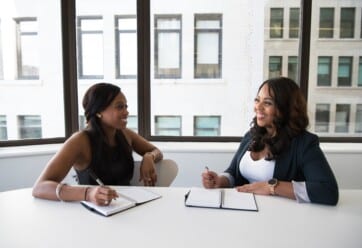 Two employees sit down to discuss and take notes