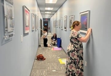 Art teachers from Stafford County Public Schools hand artwork in hallway.