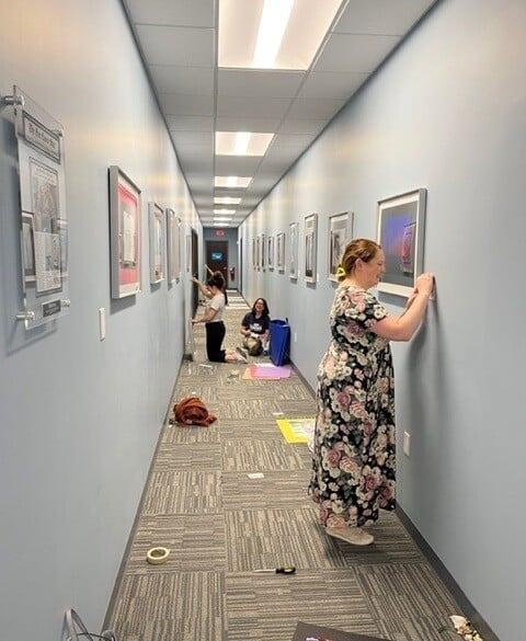Art teachers from Stafford County Public Schools hand artwork in hallway.