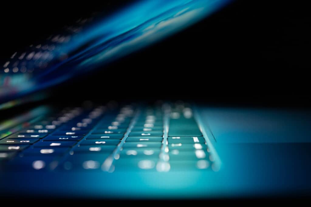 Laptop partially closed with keyboard illuminated against dark backdrop