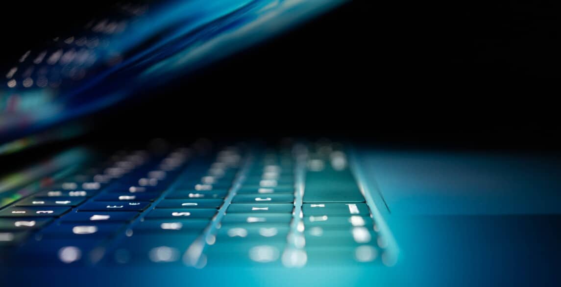 Laptop partially closed with keyboard illuminated against dark backdrop