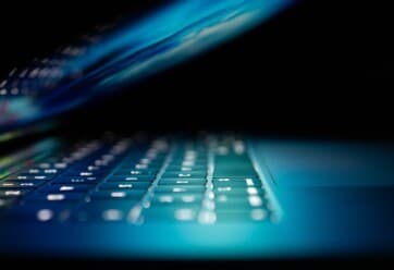 Laptop partially closed with keyboard illuminated against dark backdrop