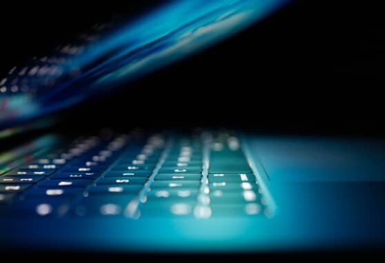 Laptop partially closed with keyboard illuminated against dark backdrop