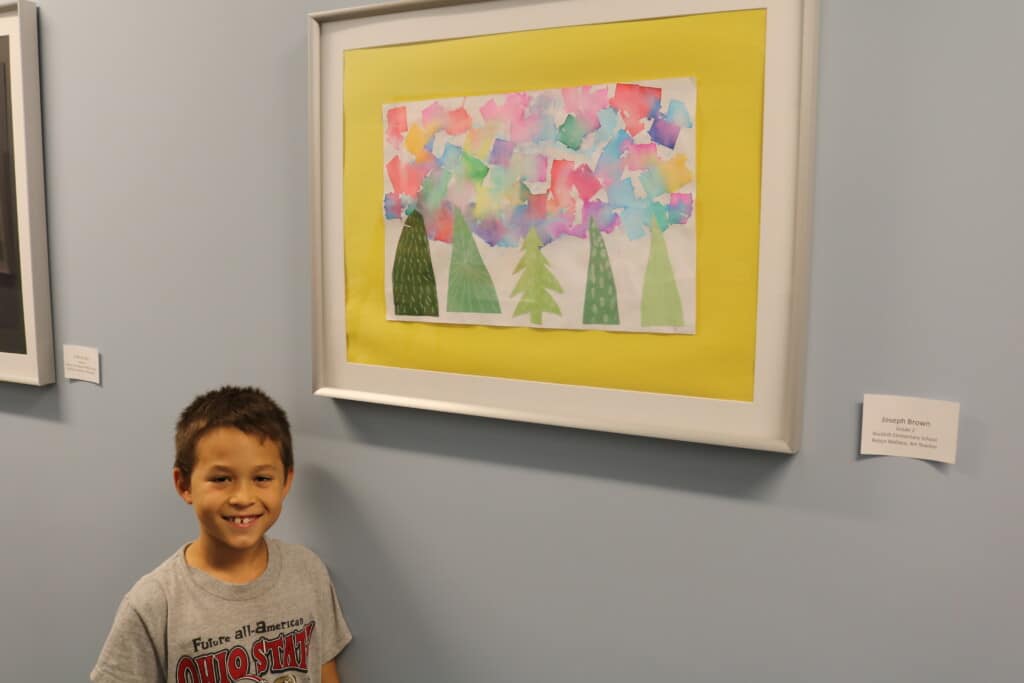 Art on display with the student artist standing next to it. 