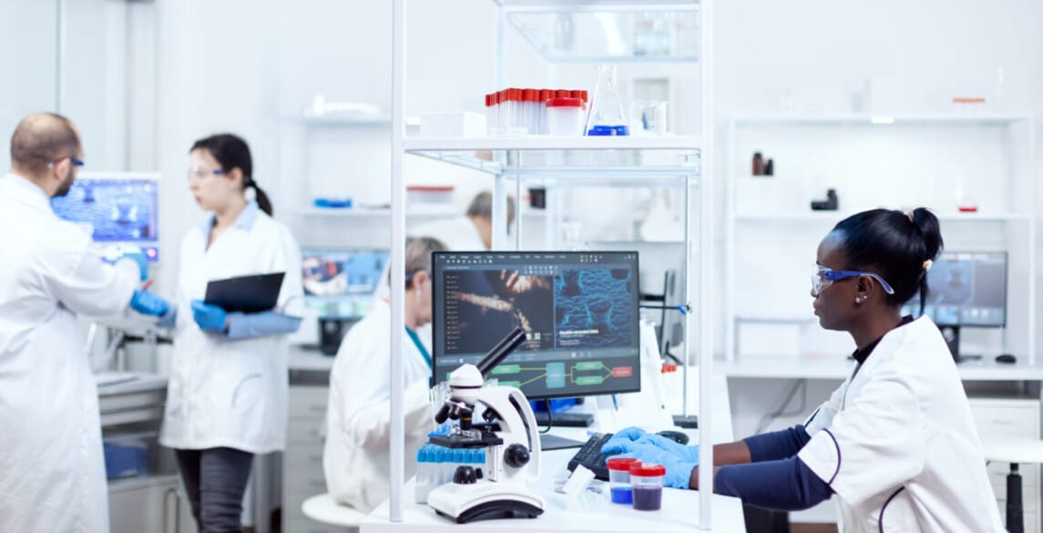 scientist sitting at her workplace in modern facility for medicine industry. Black healthcare researcher in biochemistry laboratory wearing sterile equipment.