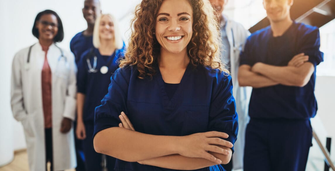 Young female doctor smiling while standing in a hospital corridor with a diverse group of staff in the background