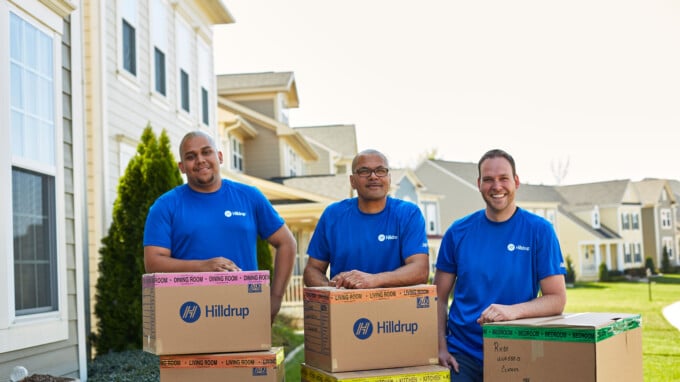 Image of three male Hilldrup movers with boxes standing outside a home